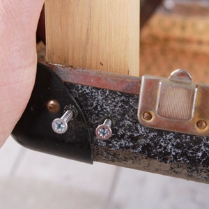 May include: Close-up of a black suitcase with a metal latch and two screws. The suitcase is being held by a hand.