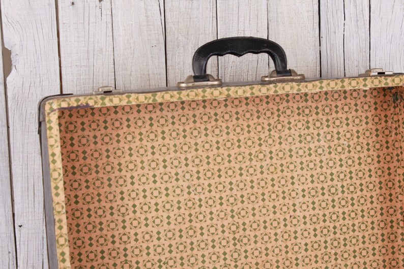 May include: An empty vintage suitcase with a black handle and a brown and green patterned lining.