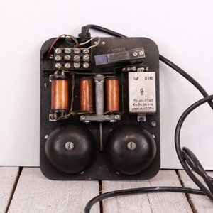 May include: Close-up of the back of a vintage black rotary phone with exposed wiring, two black bells, and a capacitor labelled "1uF 24V2".