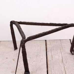 May include: A rustic, dark brown metal trivet with a triangular top and three legs. The trivet is made of wrought iron and has a rough, textured surface. It is designed to hold hot pots and pans.