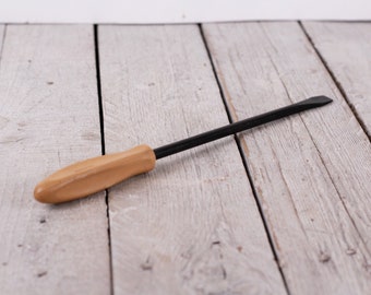 May include: A black and brown wooden handled tool with a flat, pointed tip. The tool is lying on a light wood surface.