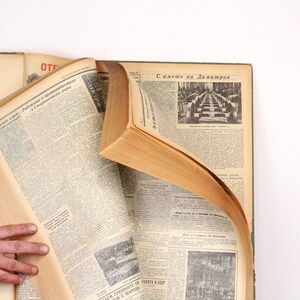 May include: A vintage book with a brown leather cover and yellowed pages. The book is open to a page with text in a foreign language. The book is lying on a white surface.