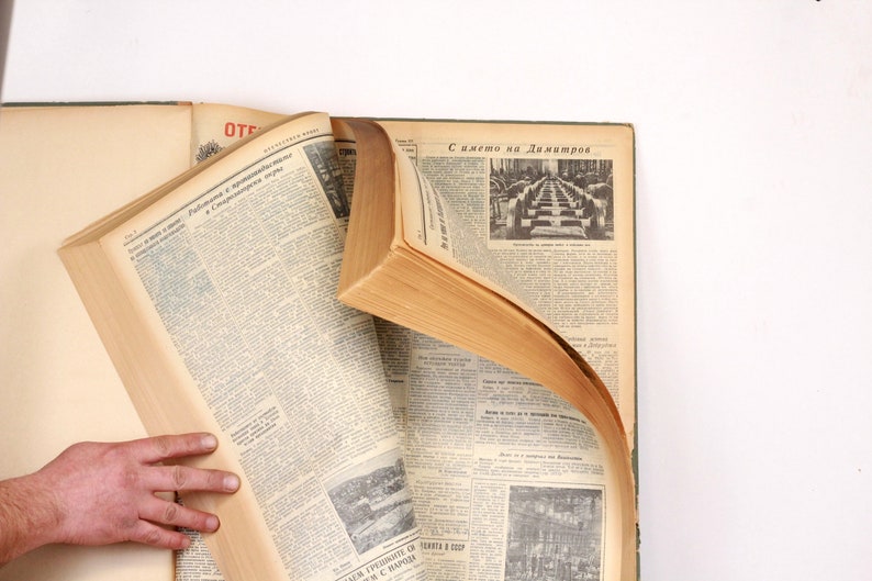 May include: A vintage book with a brown leather cover and yellowed pages. The book is open to a page with text in a foreign language. The book is lying on a white surface.