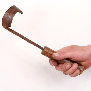 Könnte beinhalten: Ein rostiges Metall-Handwerkzeug mit einem Holzgriff. Das Werkzeug hat eine gebogene Klinge und wird zum Graben oder Jäten verwendet.