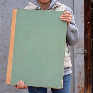 May include: A person holding a large, green, rectangular board with a wooden frame. The board is blank and has a smooth surface.