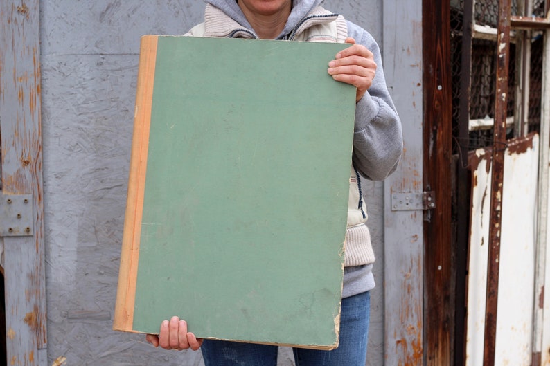 May include: A person holding a large, green, rectangular board with a wooden frame. The board is blank and has a smooth surface.