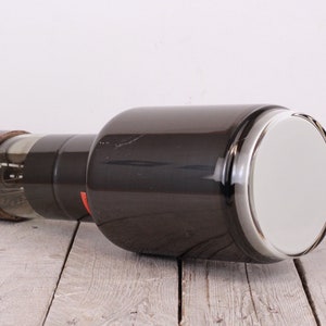 Może przedstawiać: Duża, ciemnoszara lampa próżniowa z okrągłym, białym szklanym ekranem na jednym końcu i brązową podstawą z metalowym złączem pinowym na drugim końcu.