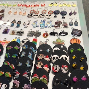 May include: Assortment of colorful cartoon character earrings on black card displays. The earrings feature characters like Elmo, Mickey Mouse, the Teenage Mutant Ninja Turtles, and more.