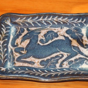May include: A blue ceramic serving dish with a white glaze and a raised design of a deer with antlers in a leafy pattern.