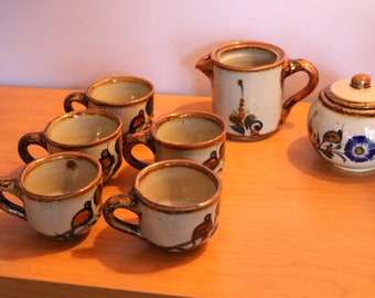 May include: A set of six brown and white ceramic teacups with floral and bird designs, a matching creamer, and a sugar bowl with a lid.