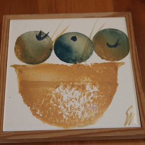 May include: A hand-painted ceramic tile with a yellow bowl and three green and blue fruit. The tile is framed in wood.
