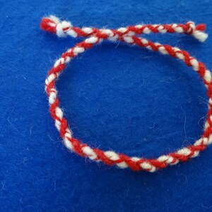 May include: A red and white braided string bracelet on a blue background.