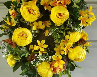 May include: A yellow floral wreath with a variety of yellow flowers, including peonies, roses, and lilies. The wreath is made with artificial flowers and greenery.