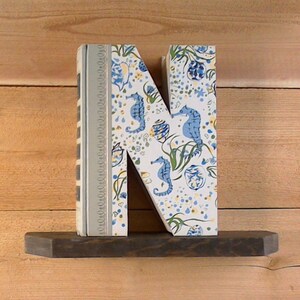 May include: A white letter N with a blue and yellow seahorse pattern. The letter is standing on a dark brown shelf.