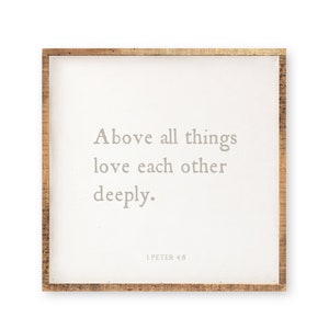 May include: A square wall sign with a natural wood frame and a white center panel. The text in gray reads: Above all things love each other deeply. 1 PETER 4:8. The design features a clean, simple layout with centered lettering on a flat surface.
