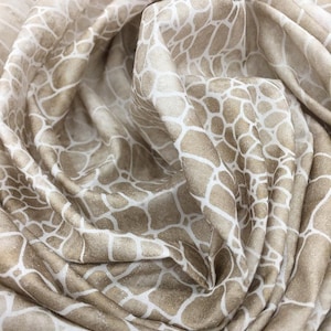 May include: A close-up of a beige fabric with a white geometric pattern. The fabric is soft and has a subtle sheen.