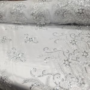 Könnte beinhalten: Weißer Netzstoff mit silbernen Pailletten, die in einem Blumenmuster gestickt sind.