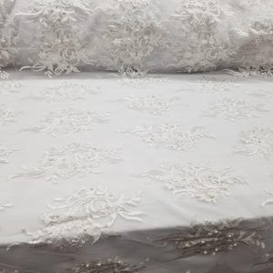 Tecido de renda branco de 57 polegadas com bordado de pérolas e flores sobre tule, ideal para toalhas de mesa, fantasias, decorações e caminhos de mesa. Vendido por metro.