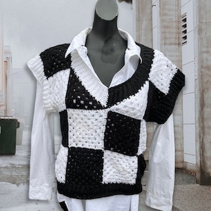 May include: A black and white crocheted vest with a checkered pattern. The vest has a v-neck and short sleeves.