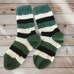 May include: A pair of green, white, and black striped crocheted socks. The socks are made with a textured stitch and have a ribbed cuff.