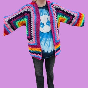 Peut inclure: Un cardigan en crochet color&eacute; avec un motif arc-en-ciel. Le cardigan est ouvert &agrave; l'avant et a des manches longues.