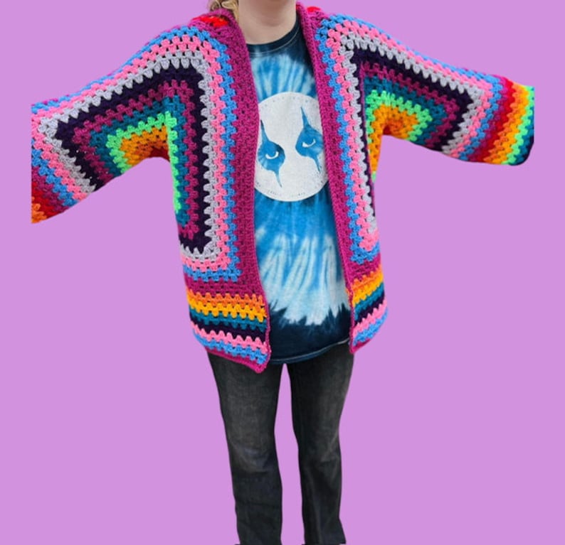 Peut inclure: Un cardigan en crochet color&eacute; avec un motif arc-en-ciel. Le cardigan est ouvert &agrave; l'avant et a des manches longues.