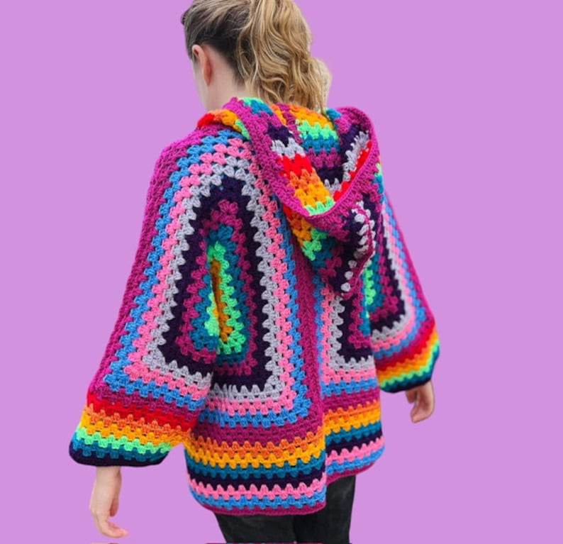 Peut inclure: Un cardigan &agrave; capuche en crochet color&eacute; avec un motif de rayures arc-en-ciel. Le cardigan est fait de plusieurs couleurs, dont le rose, le violet, le bleu, le vert, le jaune, l'orange et le rouge.