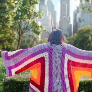 May include: A colorful crocheted cardigan with a geometric pattern in shades of purple, white, red, orange, and yellow. The cardigan is open in the front and has long sleeves.