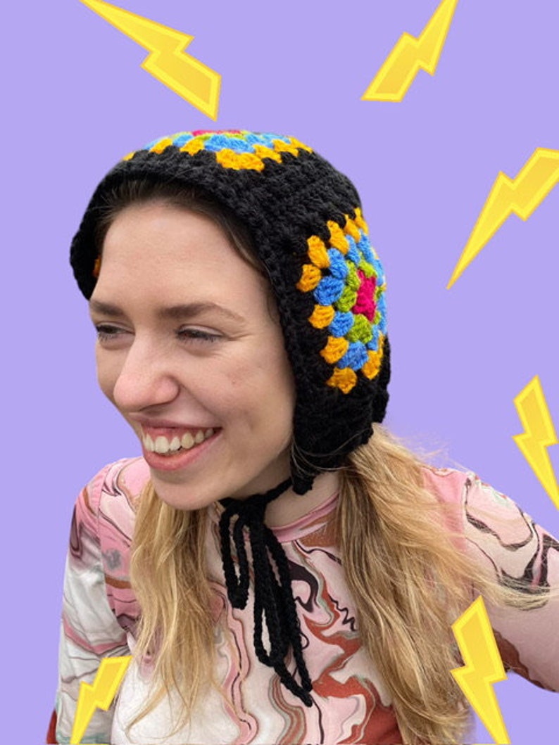May include: A black crochet hat with a colorful granny square pattern. The hat has a long tie that can be worn around the neck.