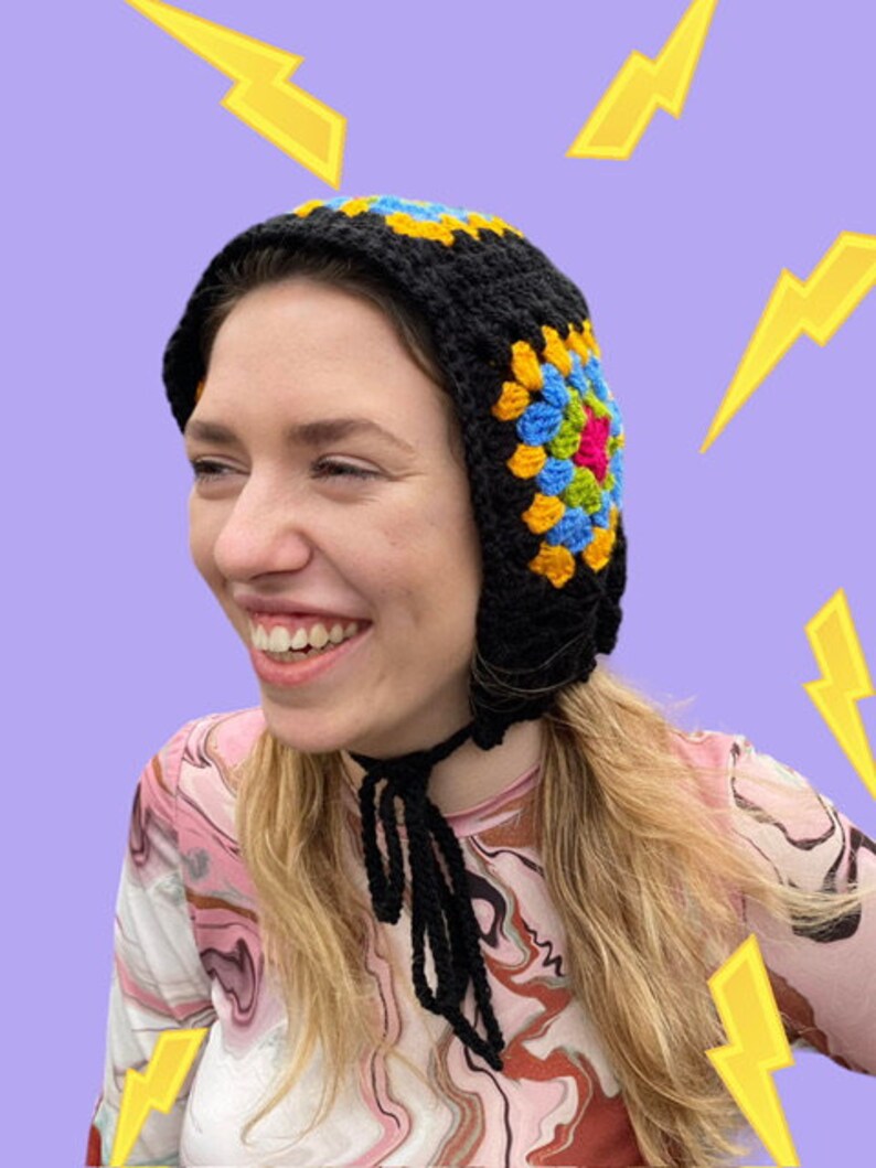 May include: A black crochet hat with a colorful granny square design. The hat has a long tie that can be worn around the neck.