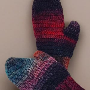 May include: A pair of hand-crocheted mittens featuring a variegated yarn pattern that transitions through shades of deep purple, vibrant magenta, bright red, and teal blue. The mittens have a ribbed cuff and a thumb section on each side.