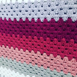 Könnte beinhalten: Eine gehäkelte Decke mit einem Chevron-Muster in den Farben Weiß, Grau, Rosa und Rot.