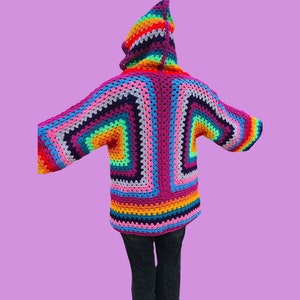 Peut inclure: Un cardigan &agrave; capuche en crochet color&eacute; avec un motif arc-en-ciel. Le cardigan est fait de plusieurs couleurs, dont le rose, le violet, le bleu, le vert, le jaune, l'orange et le rouge.
