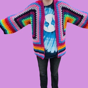 Peut inclure: Un cardigan en crochet arc-en-ciel avec un devant large et ouvert et des manches longues. Le cardigan est fait avec une vari&eacute;t&eacute; de couleurs, y compris le rouge, l'orange, le jaune, le vert, le bleu, l'indigo et le violet.
