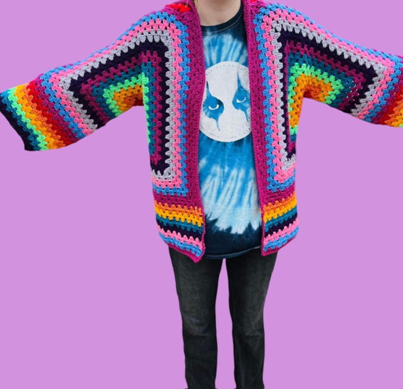 Peut inclure: Un cardigan en crochet arc-en-ciel avec un devant large et ouvert et des manches longues. Le cardigan est fait avec une vari&eacute;t&eacute; de couleurs, y compris le rouge, l'orange, le jaune, le vert, le bleu, l'indigo et le violet.