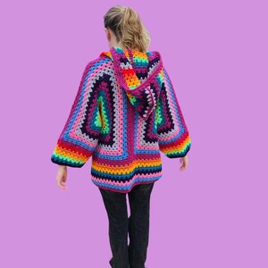 Peut inclure: Un cardigan &agrave; capuche en crochet color&eacute; avec un motif de rayures arc-en-ciel. Le cardigan est fait de plusieurs couleurs, dont le rose, le violet, le bleu, le vert, le jaune et l'orange.