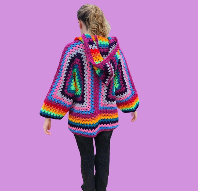 Peut inclure: Un cardigan &agrave; capuche en crochet color&eacute; avec un motif de rayures arc-en-ciel. Le cardigan est fait de plusieurs couleurs, dont le rose, le violet, le bleu, le vert, le jaune et l'orange.