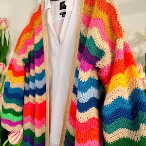 May include: A rainbow striped crochet cardigan with a wavy pattern. The cardigan is open at the front and has long sleeves.