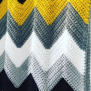 Puede incluir: Una manta de crochet en chevron en negro, gris, blanco y amarillo.