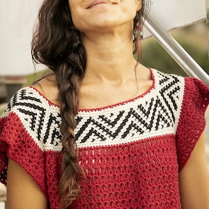 Puede incluir: Una mujer con el pelo largo y castaño trenzado a un lado lleva un top de crochet rojo con un patrón geométrico blanco y negro alrededor del escote.