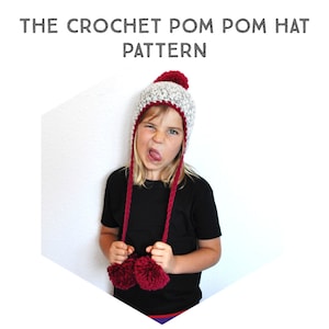 Peut inclure: Un enfant portant un bonnet en crochet gris et rouge avec des pompons et des rabats d'oreilles. Le bonnet a une bordure en crochet rouge et des liens. L'enfant porte un t-shirt noir.