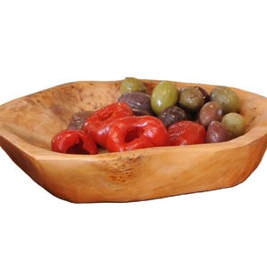 Può includere: Una ciotola di legno piena di olive e peperoni rossi. La ciotola è marrone chiaro e ha un aspetto naturale e rustico. Le olive sono verdi, nere e viola. I peperoni rossi sono di un rosso brillante.