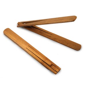 Puede incluir: Tres perchas de madera con acabado natural dispuestas sobre fondo blanco. Cada percha tiene forma rectangular con una ranura en el centro y un extremo dentado para colgar la ropa. Las perchas son de madera de color marrón claro.