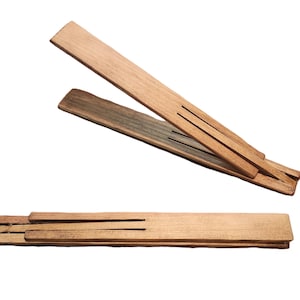May include: Three wooden, rectangular, slotted trivets in varying shades of brown. One trivet is fully assembled, while the other two are partially assembled, with one angled upwards. The trivets are made of natural wood.