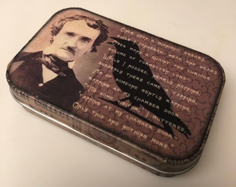 May include: A vintage tin box with a brown and black design featuring a portrait of Edgar Allan Poe and a raven. The box has a quote from Poe's poem "The Raven" printed on it: "Once upon a midnight dreary, while I pondered, weak and weary, Over many a quaint and curious volume of forgotten lore— While I nodded, nearly napping, suddenly there came a tapping, As of someone gently rapping, rapping at my chamber door."