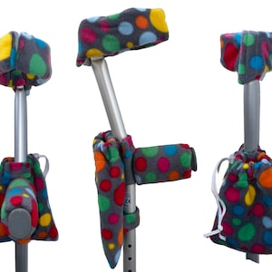 May include: A grey crutch with a colourful polka dot pattern covering the handle, top, and lower portion. The crutch has a grey fleece bag attached to the lower portion.