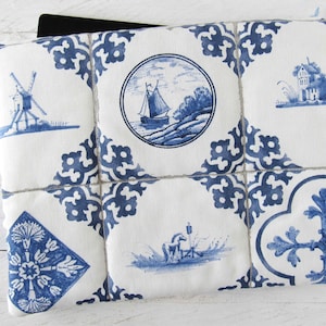 May include: A white and blue patterned laptop sleeve featuring a Delftware design. The sleeve has a repeating pattern of blue floral motifs and framed scenes of windmills, sailboats, and houses. The sleeve is designed to protect a laptop or tablet.