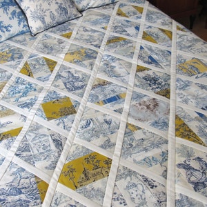 May include: A white quilt with a diamond pattern made from blue and yellow fabric. The quilt is made of multiple squares of fabric sewn together to create a diamond pattern. The quilt is made with a white background and blue and yellow fabric.