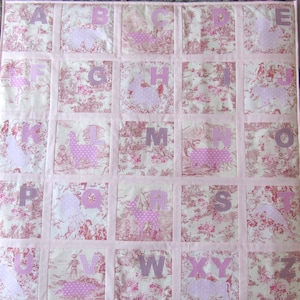 Könnte beinhalten: Ein rosa-cremefarbener Alphabet-Quilt mit jedem Quadrat mit einem Buchstaben und einer Tiersilhouette. Die Buchstaben sind in einem Karomuster und die Tiere haben ein Tupfenmuster. Der Hintergrund hat ein Toile-Muster.