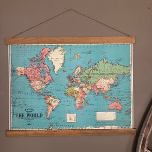 Pu&ograve; includere: Una mappa del mondo vintage in una cornice di legno. La mappa &egrave; blu con continenti rosa, verdi e gialli. La mappa &egrave; intitolata "Racons Standard Map The World On Mercator Projection".